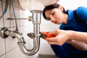 A plumber uses a wrench to repair a leaking sink drain pipe beneath a faucet.